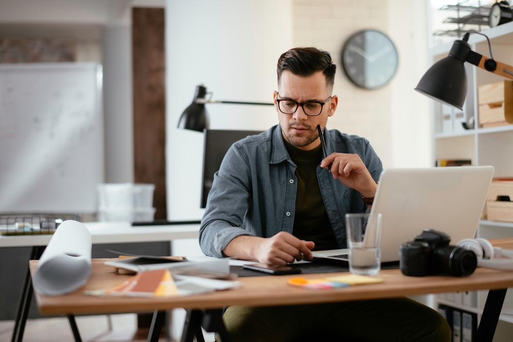 a man sitting at a desk holding a pen to his mouth thinking while he works from home