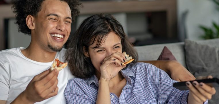 Happy-couple-watching-tv-while-eating-pizza-min