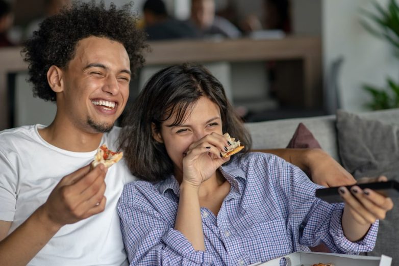 Happy-couple-watching-tv-while-eating-pizza-min